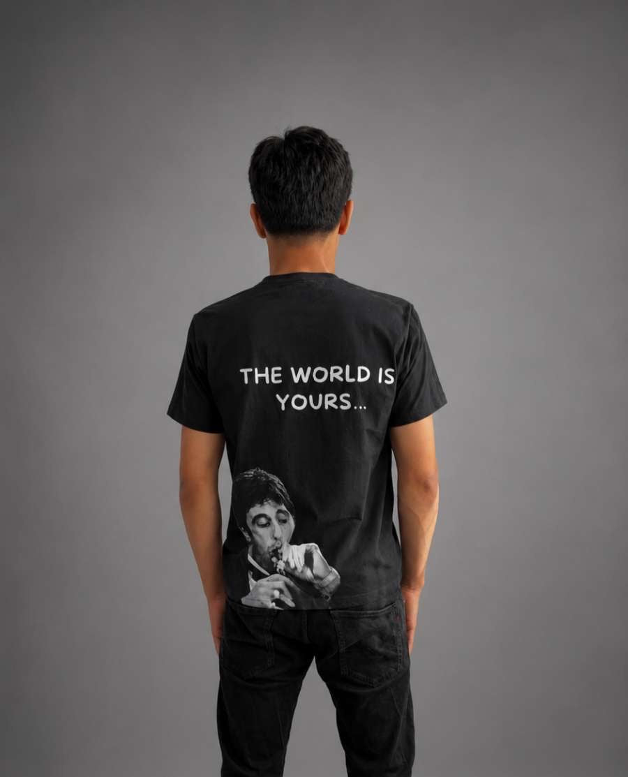 Svart T-shirt med texten "The World is Yours" från RISKTAKERS, visad på modell.
