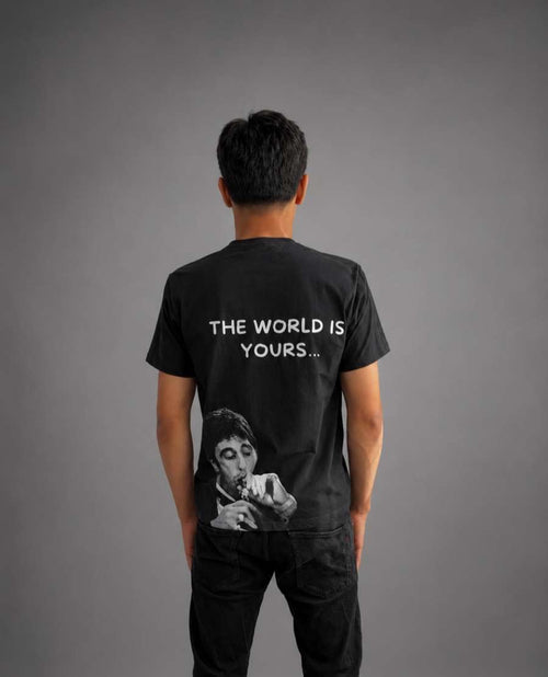 Svart T-shirt med texten "The World is Yours" från RISKTAKERS, visad på modell.