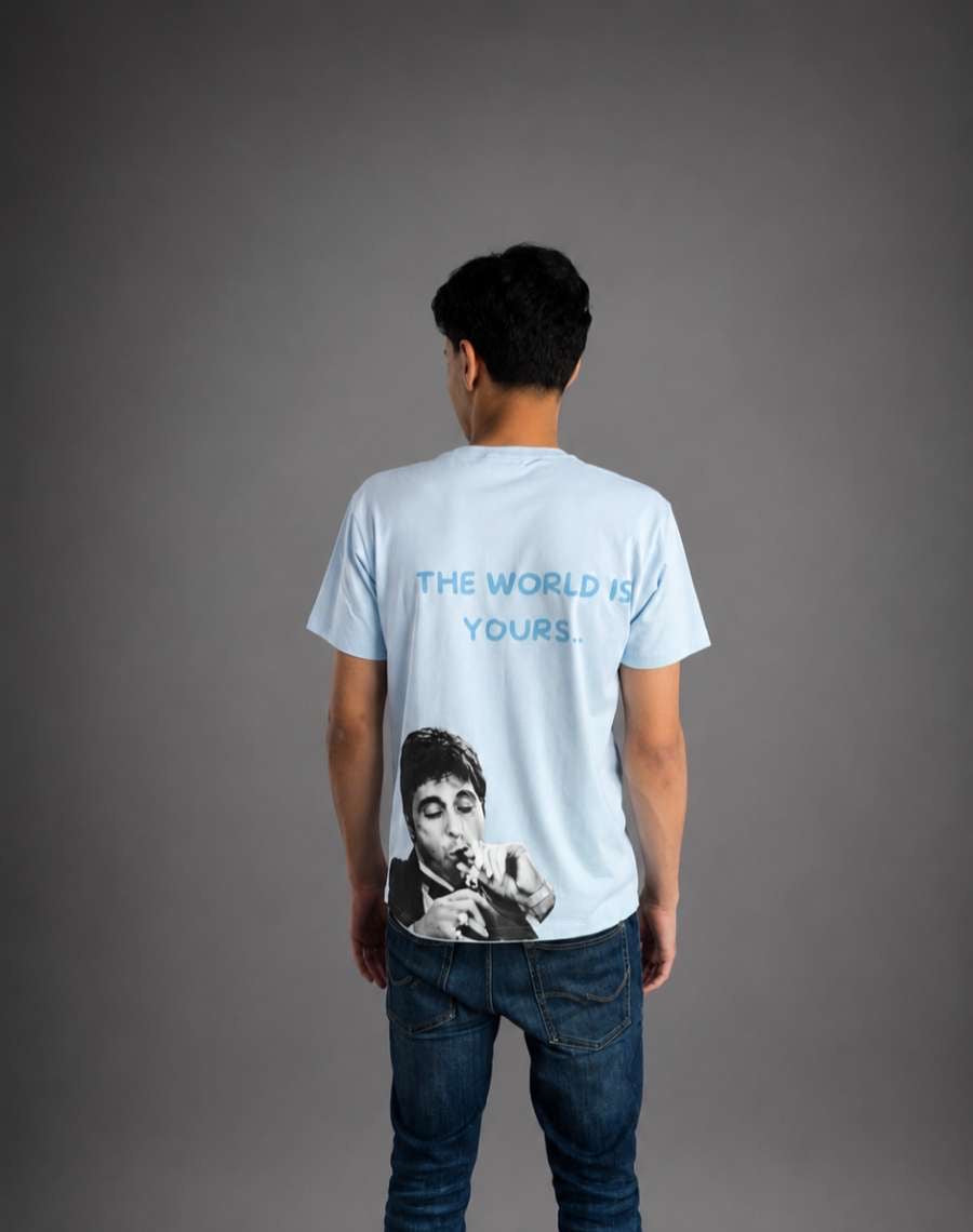 Blå mineralfärgad t-shirt med texten "The World Is Yours" från RISKTAKERS, visad på modell i bild.